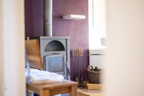 A cozy room with a fireplace, a wooden chair, a floor lamp, and a shelf with candles. - Chasa Patgific: Cozy 3-Room Holiday Apartment with Wood Stove and Stunning Garden in Ramosch (Ramosch)