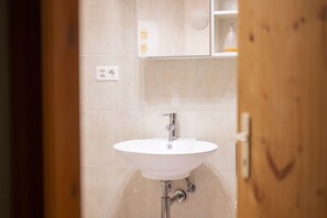 A bathroom with a white sink, a mirror, and a shelf with toiletries.