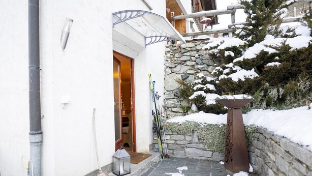 Un espacio exterior cubierto de nieve con un muro de piedra, una escalera de madera y una barandilla de metal.