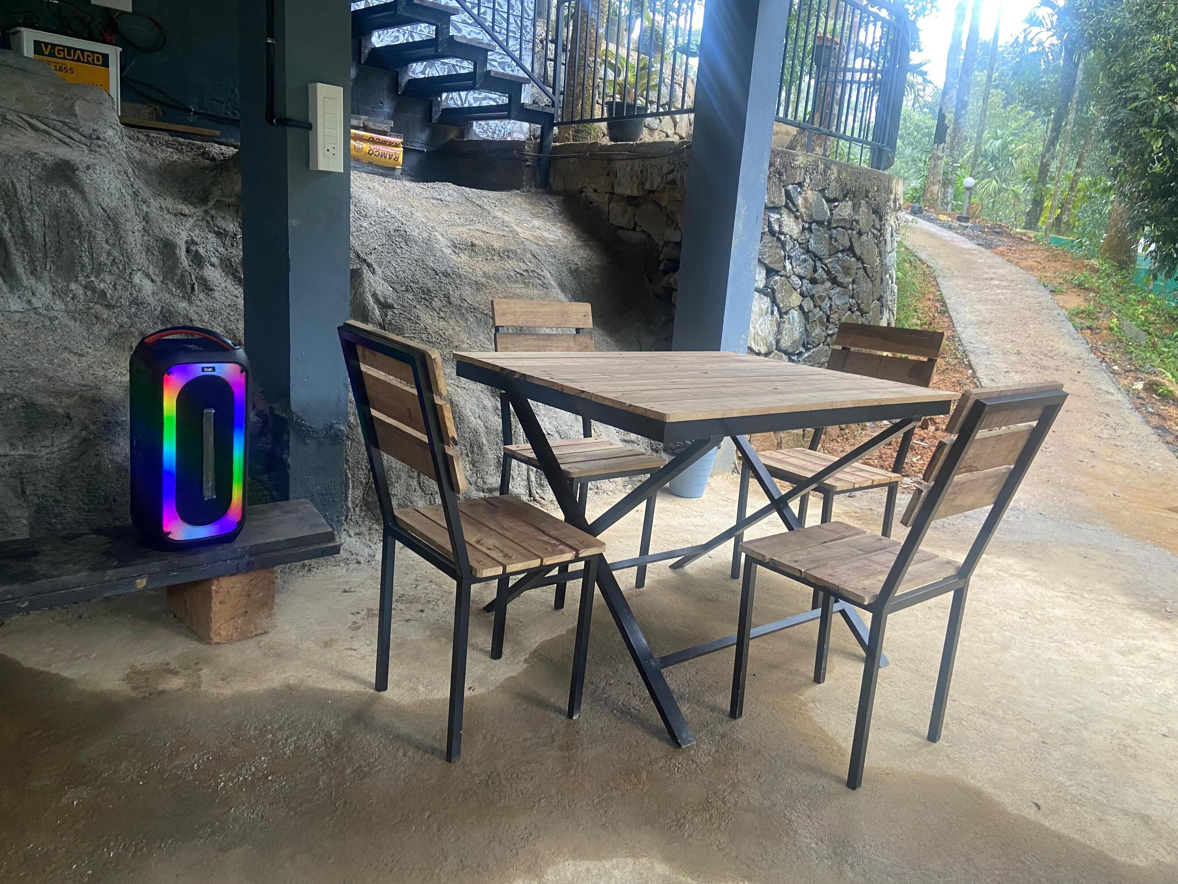 A covered outdoor seating area with a table and chairs, a neon sign, and a stone wall.