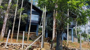 A two-story building with a balcony, surrounded by trees and a rocky area. - SR Villa - Serenity Riverside (Vythiri)