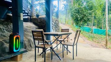 A covered outdoor seating area with a table and chairs, a stone wall, and a view of a green garden.