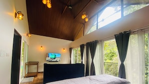 A bedroom with a bed, a television on the wall, and large windows with curtains. - SR Villa - Serenity Riverside (Vythiri)