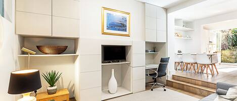 Uma sala de estar moderna com televisão de tela plana, uma área de refeições com mesa e cadeiras, e uma escadaria que leva a um espaço ao ar livre.