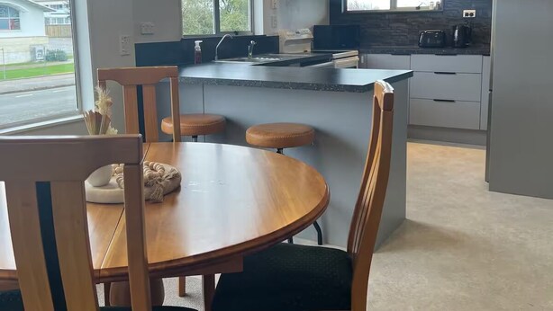 A modern kitchen with a central island, a dining area with a round table and chairs, and a view of the outside. - Heart of Windsor (Invercargill)