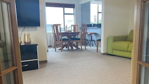 A living room with a carpeted floor, a dining area with wooden chairs and a table, a green sofa, and a TV mounted on the wall. - Heart of Windsor (Invercargill)