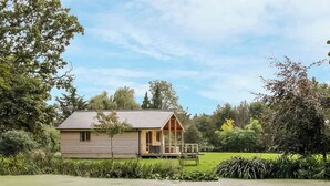 A single-story wooden cabin with a porch, surrounded by lush greenery and trees. - 2 bedroom accommodation in Oswestry (Oswestry)