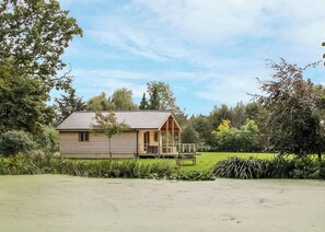 A single-story wooden cabin with a porch, surrounded by lush greenery and trees. - 2 bedroom accommodation in Oswestry (Oswestry)