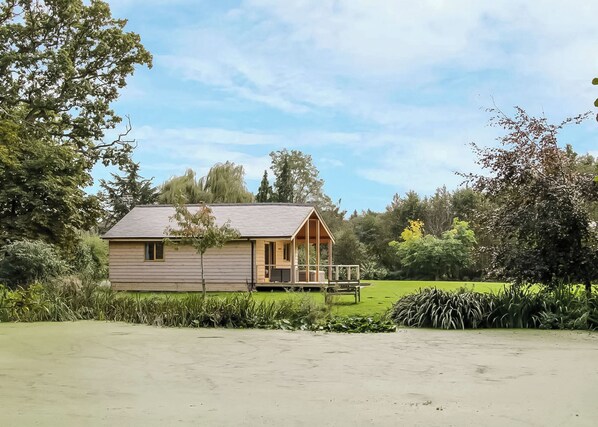 Ein einstöckiges Holzhaus mit Veranda, umgeben von üppigem Grün und Bäumen.