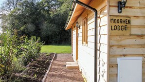 A wooden building labeled 'MOORHEN LODGE' with a pathway leading to the entrance, surrounded by greenery. - 2 bedroom accommodation in Oswestry (Oswestry)