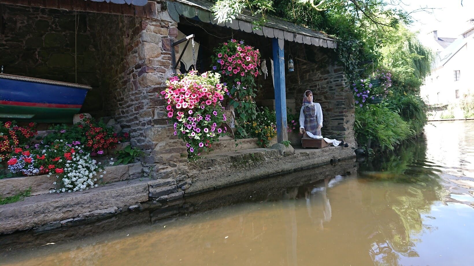 A stone building with a small porch, a wooden boat, and hanging flower baskets.