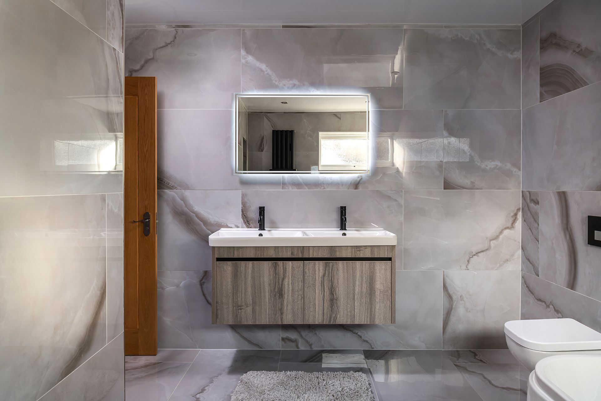 A modern bathroom with marble walls, a wooden vanity, a white sink, and a toilet.
