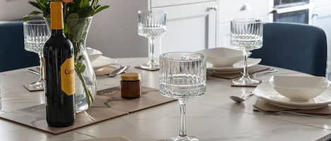 Una mesa de comedor dispuesta con copas de cristal, una botella de vino y rosas rojas en un jarrón.
