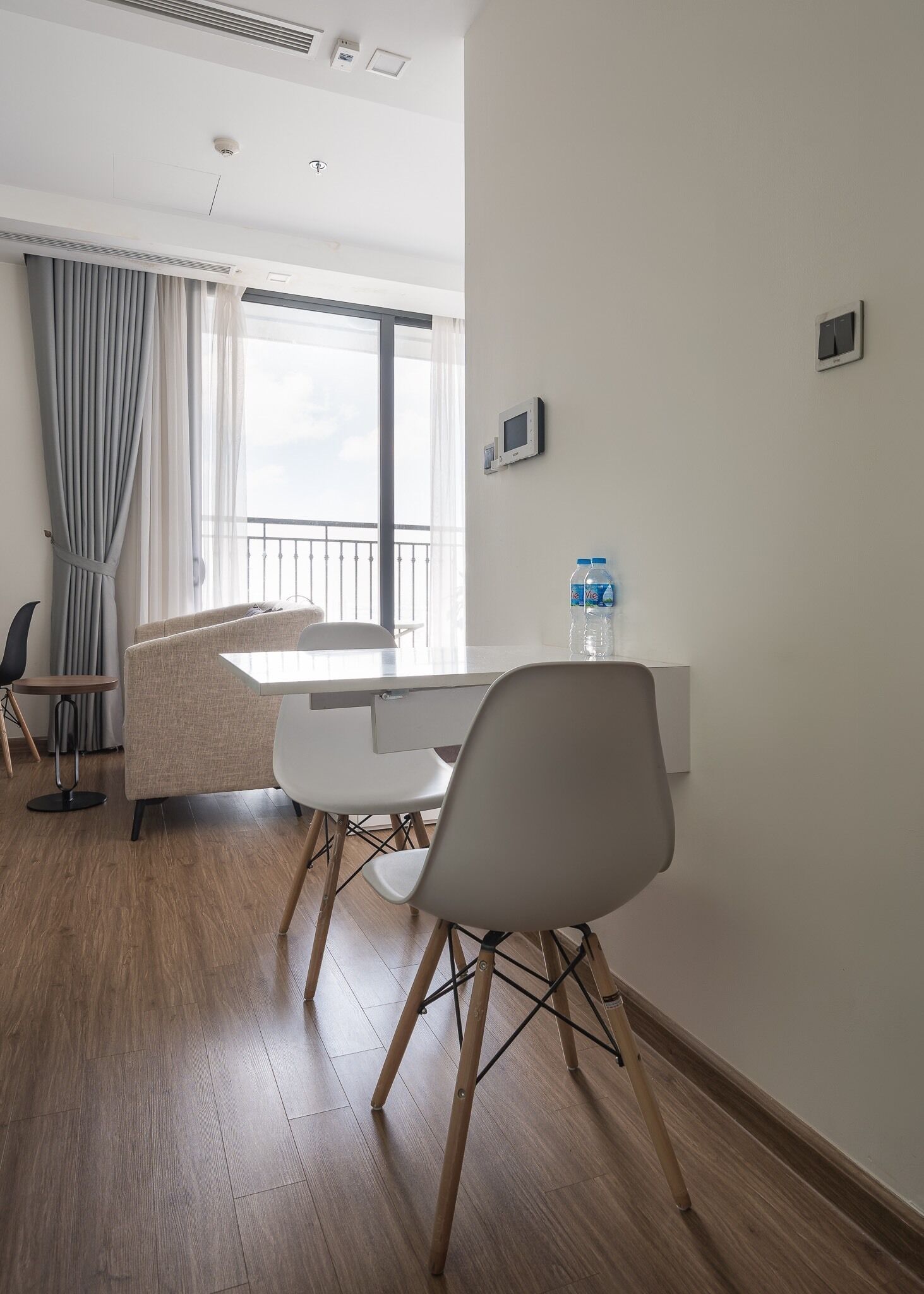 Ein modernes Hotelzimmer mit Essbereich, einem großen Fenster mit Vorhängen, einem Wasserspender und einem Thermostat an der Wand.