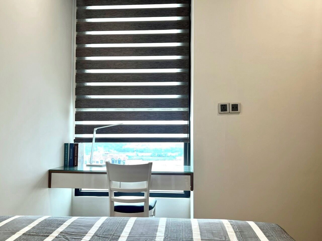 Pequeño estudio con escritorio, silla y ventana con persianas.