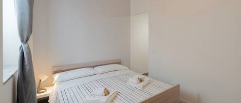 Una cama bien hecha con ropa de cama a rayas y toallas, una lámpara de noche y una cortina colgante.