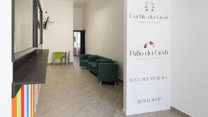 Un moderno vestíbulo de hotel con mostrador de recepción, zona de estar con asientos verdes y una pared con nombres de empresas.