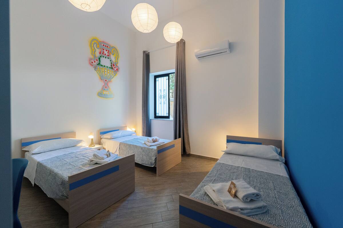 Habitación de hotel con dos camas individuales, una ventana con cortinas, un equipo de aire acondicionado y un adorno en la pared.