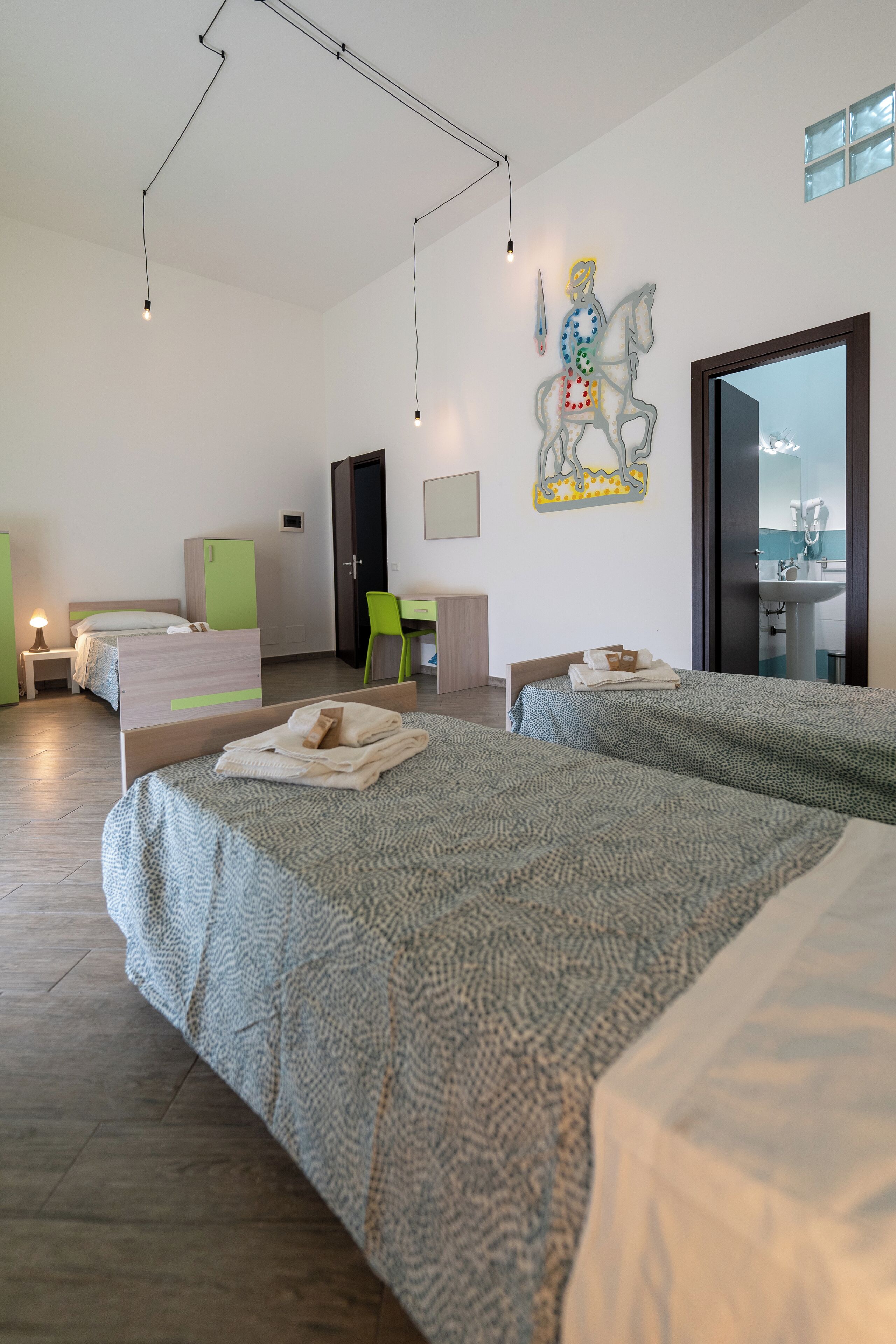 Een moderne hotelkamer met twee bedden, een bureau, een stoel en een zichtbare badkamer door een geopende deur.
