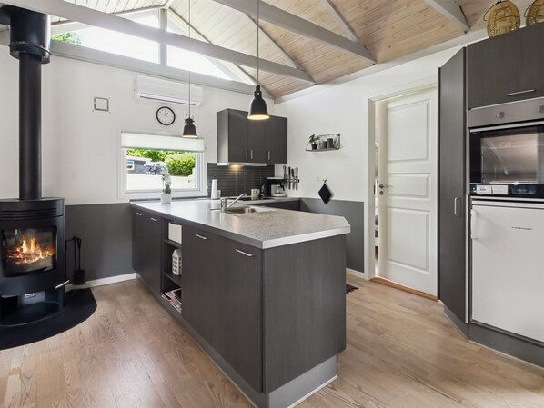 Une cuisine moderne dotée d’un îlot central, d’une cuisinière intégrée et d’une grande fenêtre donnant sur un jardin.