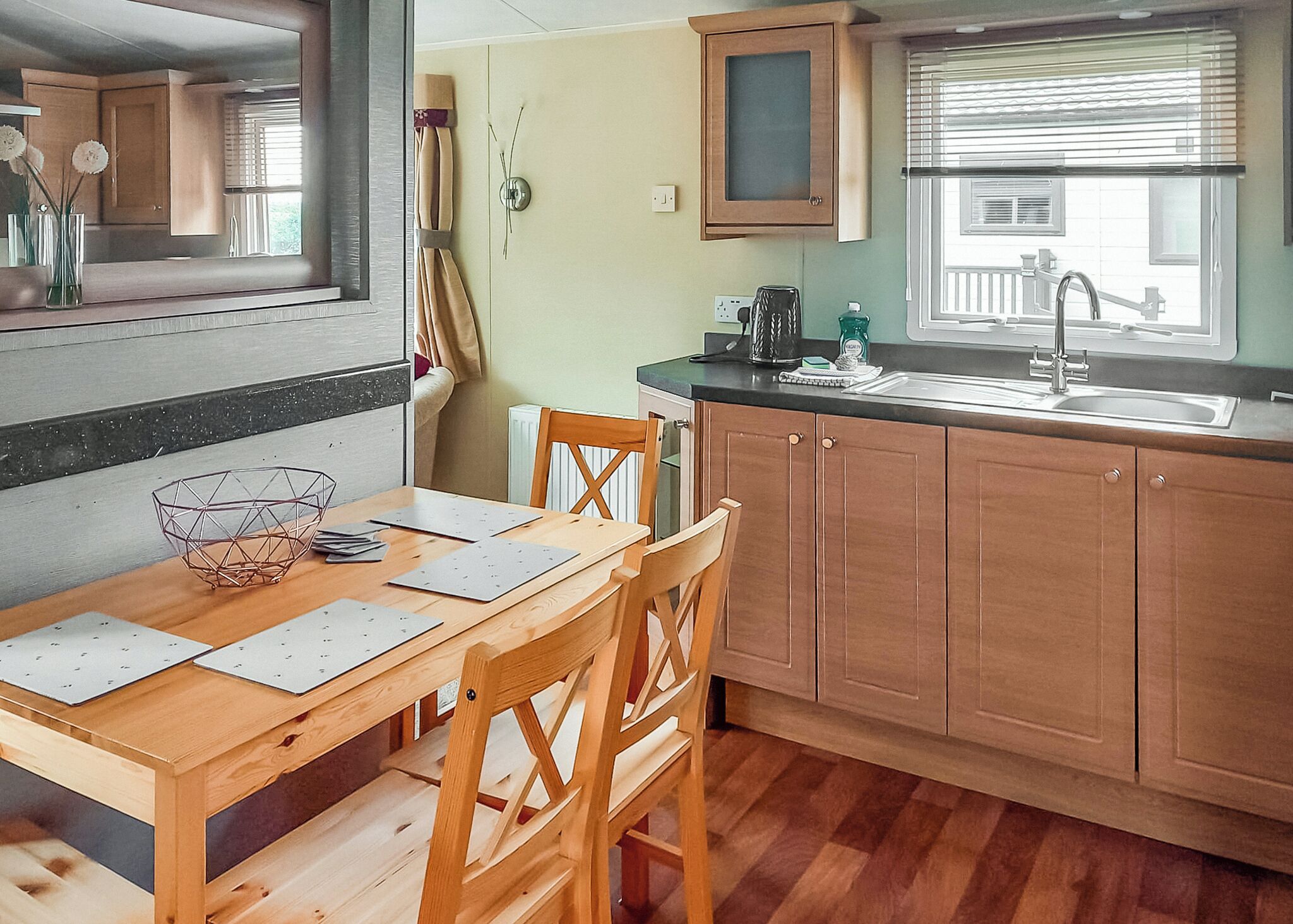 A kitchen with wooden cabinets, a dining table with chairs, a window with blinds, and a radiator.