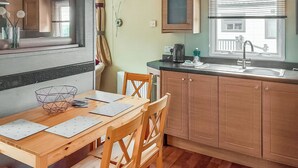 A kitchen with wooden cabinets, a dining table with chairs, a window with blinds, and a radiator.