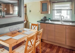 A kitchen with wooden cabinets, a dining table with chairs, a window with blinds, and a radiator.
