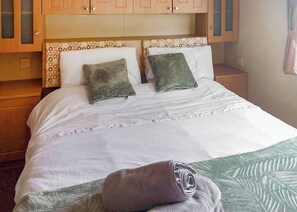 A bedroom with a bed, two pillows, a bedside table, and a nightstand.