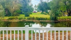 A serene lakeside view with a white fence in the foreground, a grassy area, and a small building in the distance.