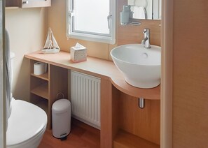 A bathroom with a white toilet, a white sink, a towel dispenser, a small trash bin, a radiator, and a window.