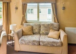 A living room with a sofa, a lamp, and a view of a house through a window.