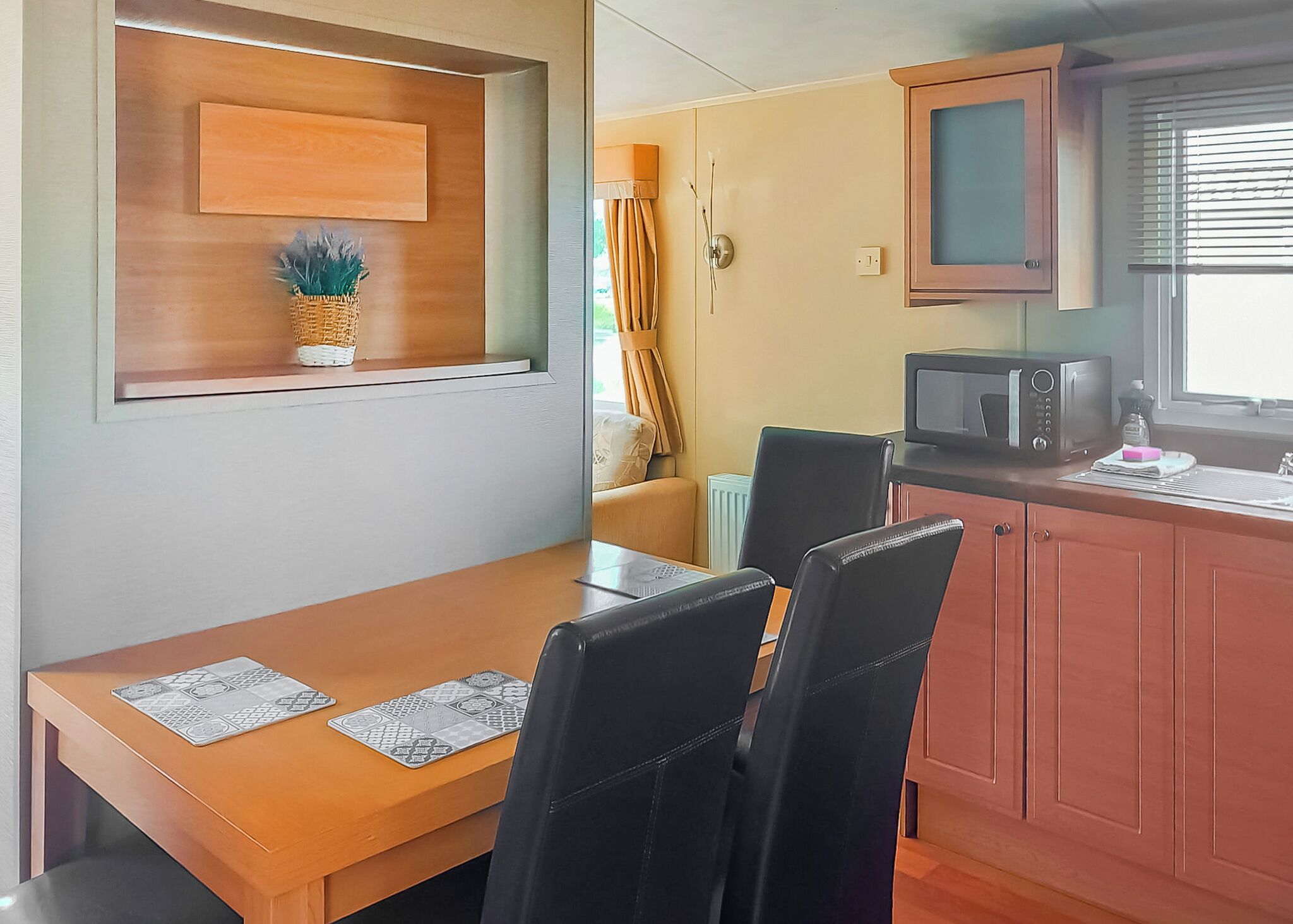 A compact kitchen with a dining table, chairs, a microwave, and a window with blinds.