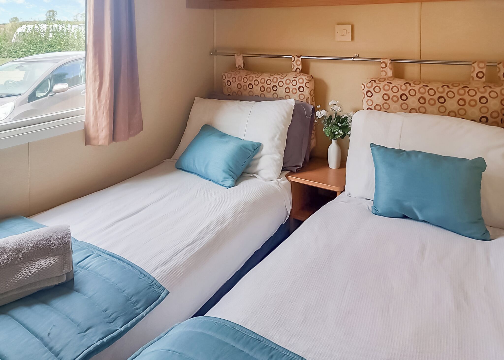 A double bed with a headboard, a bedside table with a vase, and a window with a curtain.