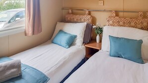 Un lit double avec une tête de lit, une table de chevet avec un vase et une fenêtre avec un rideau.