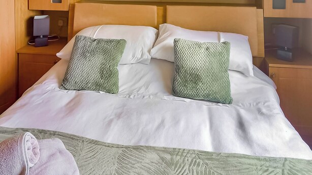 A neatly made bed with two pillows, a bedside table with a lamp, and wooden cabinets above.