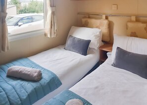 Habitación de hotel con dos camas individuales, una ventana con cortinas, una mesita de noche y vistas al exterior.