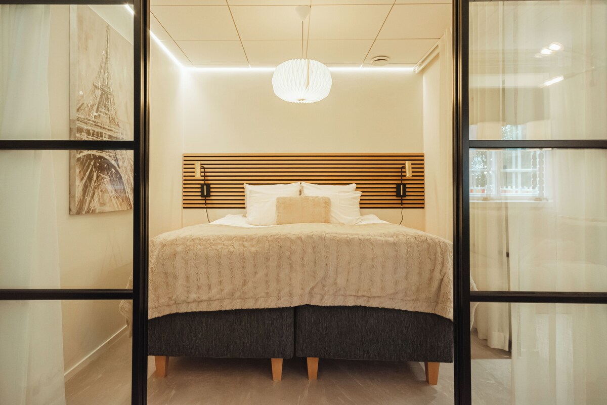 Een moderne slaapkamer met een groot bed, een houten hoofdbord en een hanglamp.