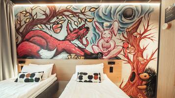A hotel room with two beds, a mural with a wolf and a rabbit, and a tree with a hedgehog.