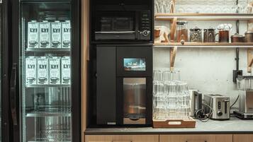 A kitchen area with a coffee machine, a microwave, and a refrigerator. There are also shelves with glassware and a coffee machine display.