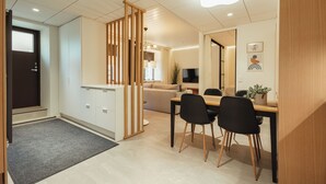 A modern living room with a sofa, a dining table with chairs, a TV, and a kitchen area with cabinets and a refrigerator.