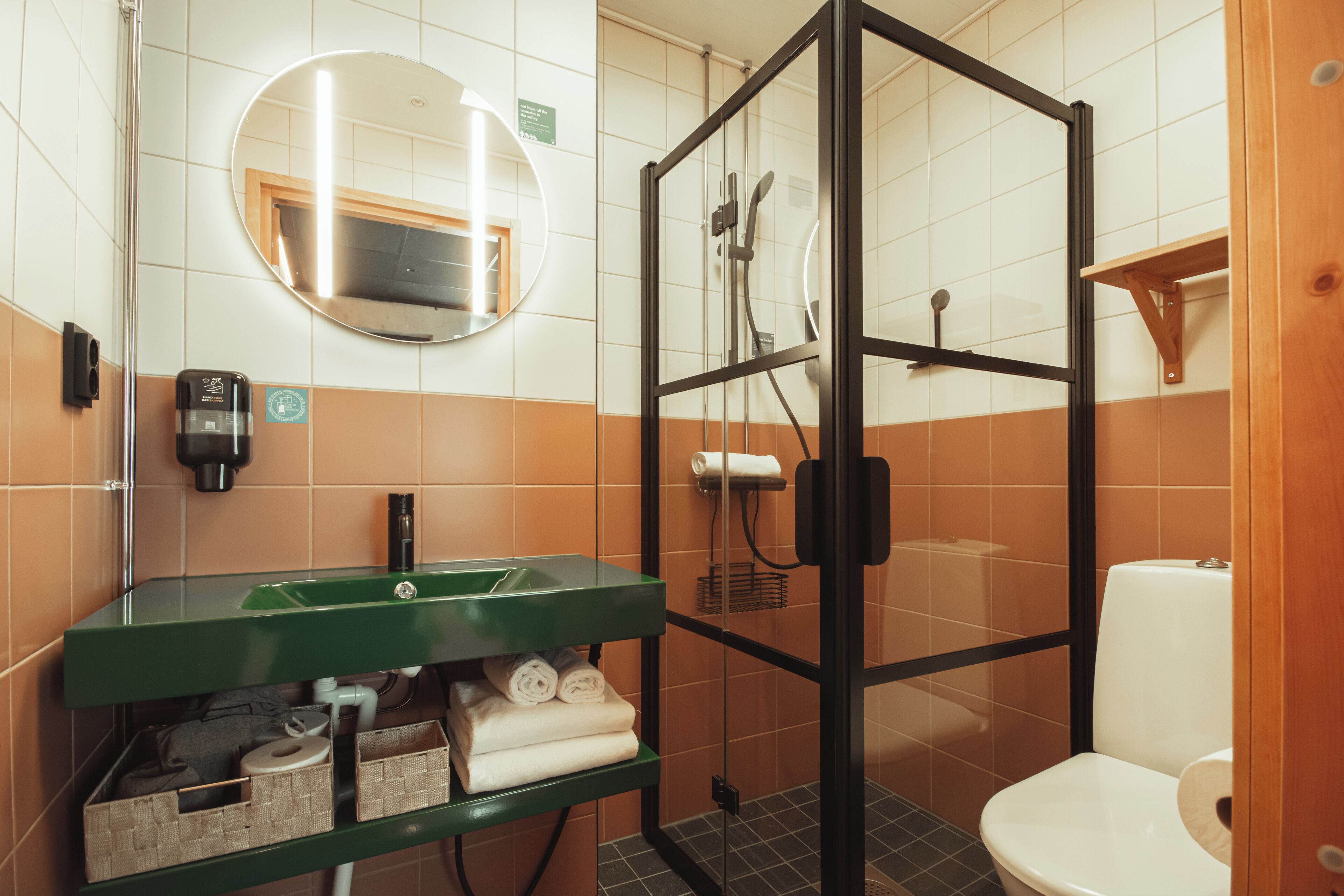 A bathroom with a glass-enclosed shower, a green sink, and a toilet.