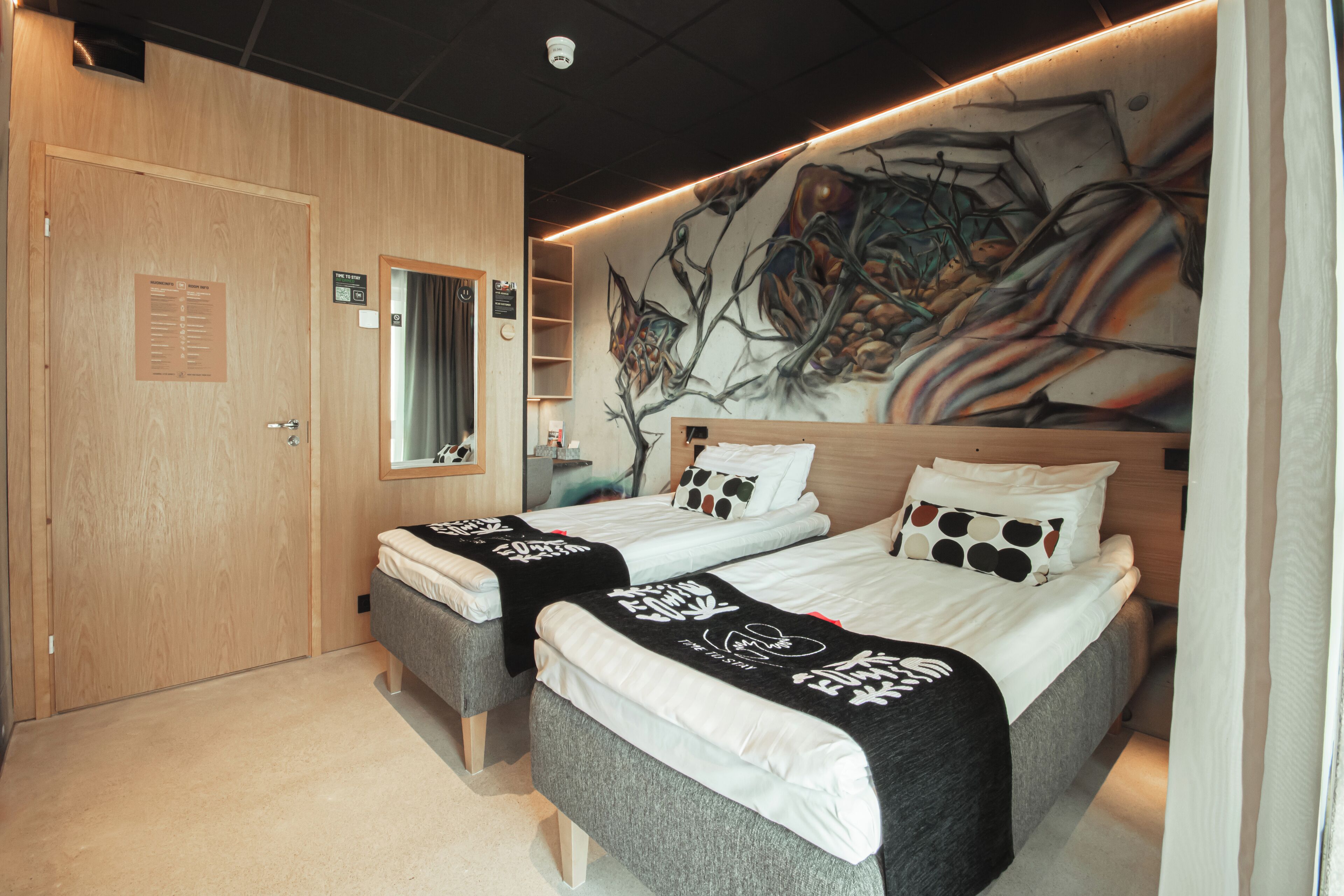 Et moderne hotelværelse med to senge, et stort vægmaleri og en trædør.