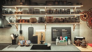 A kitchen with shelves of dishes and utensils, a sink, and a sign with instructions.