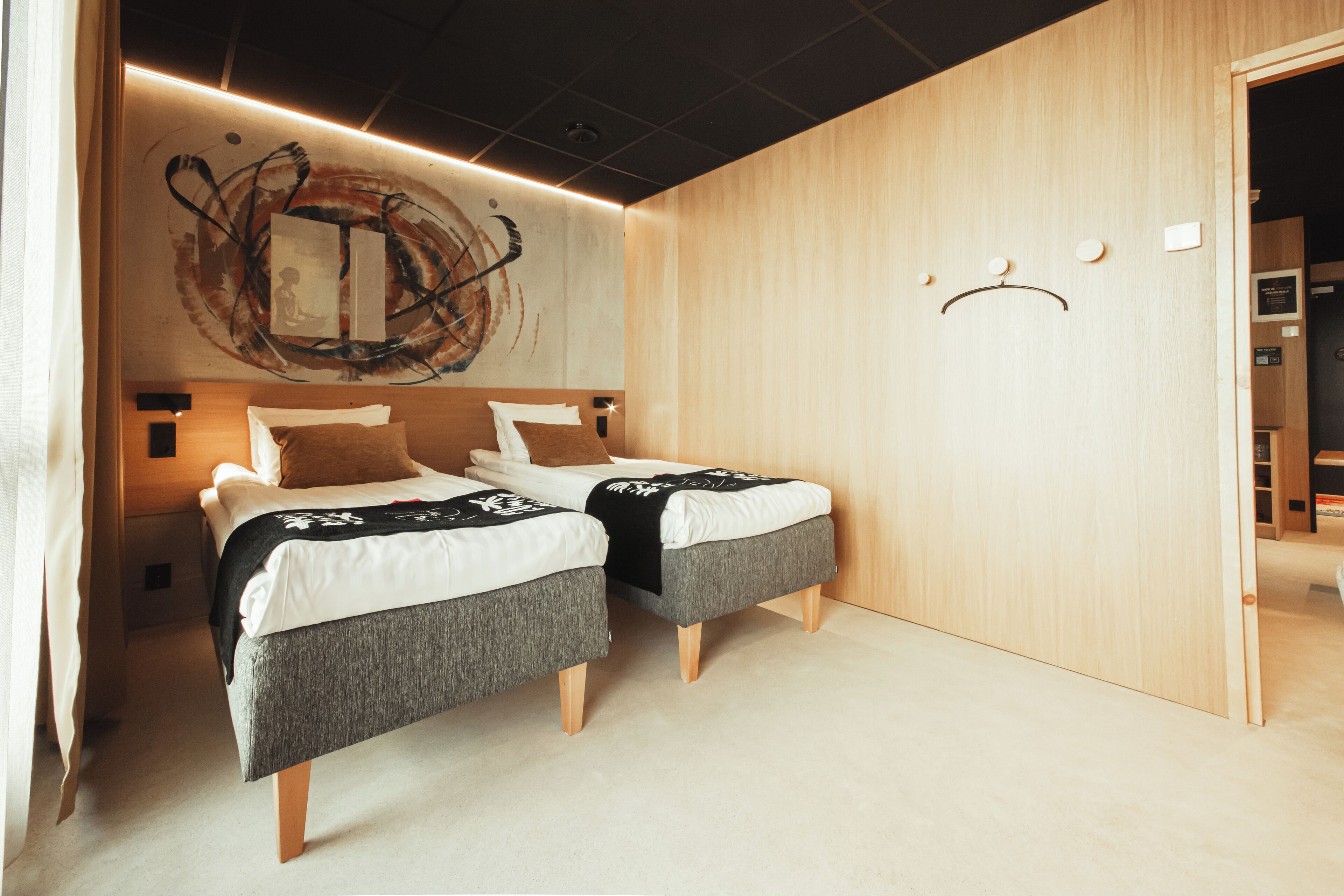 A modern bedroom with two beds, a wooden wall, and a unique abstract painting.