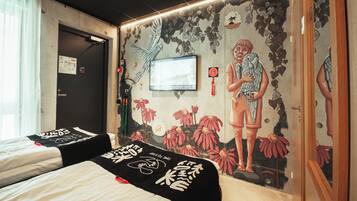 Habitación de hotel con dos camas, un mural con un pájaro y flores, un televisor y una puerta con un cartel.