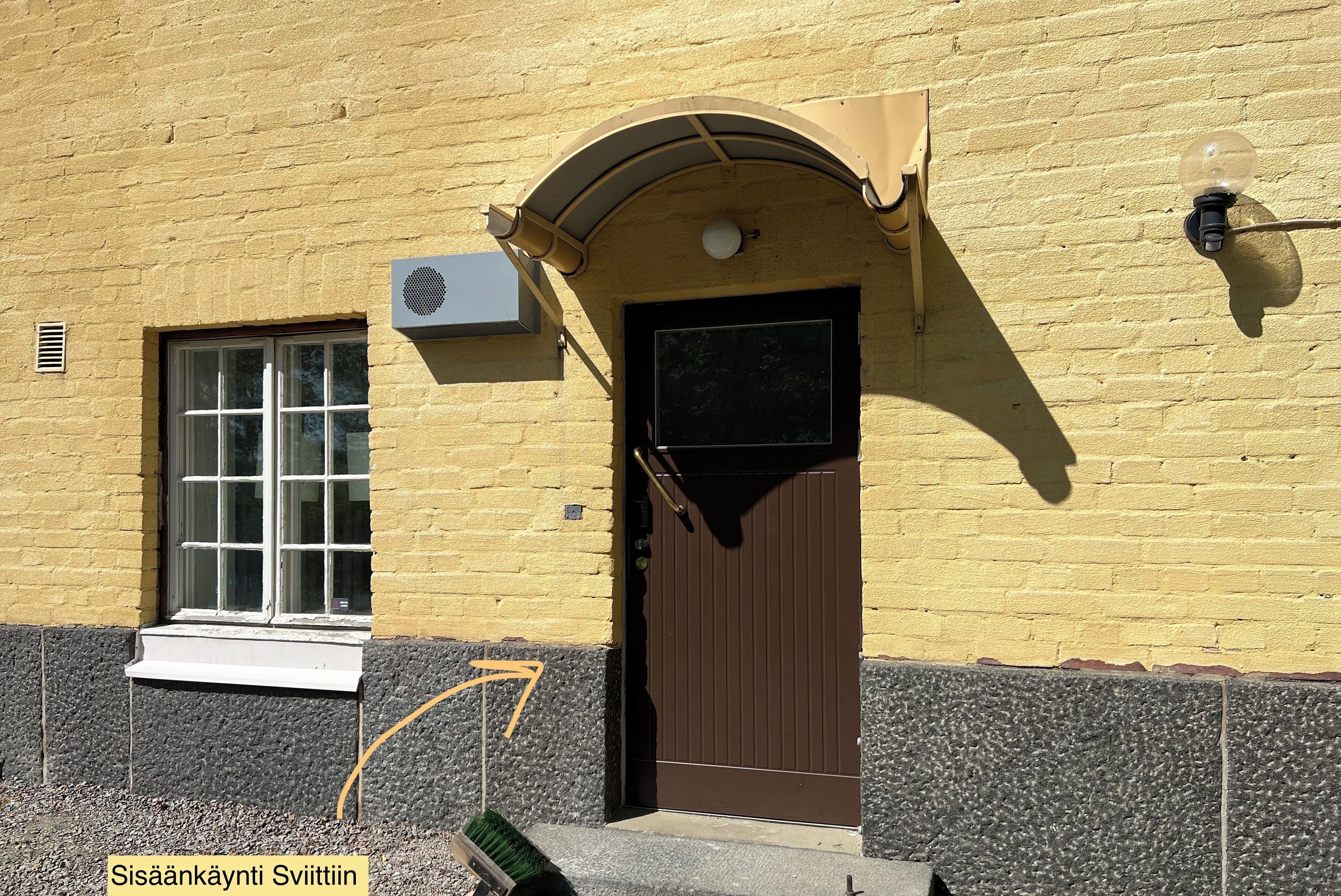 En bygning med en brun dør, et vindue og en aircondition.