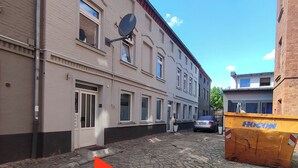 Eine Kopfsteinpflasterstraße mit Gebäuden an beiden Seiten, einer Satellitenschüssel auf einem Gebäude und einer gelben Mülltonne im Vordergrund.