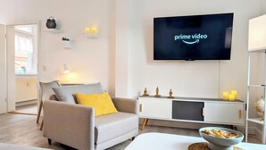 Ein modernes Wohnzimmer mit grauem Sofa, einem weißen Couchtisch und einem an der Wand befestigten Flachbildfernseher, der 'Prime Video' zeigt.