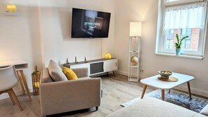 Ein modernes Wohnzimmer mit Flachbildfernseher, einer Couch, einem Couchtisch und einer kleinen Essecke.