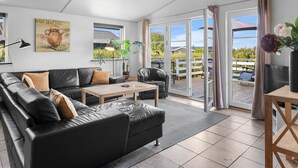 Ett modernt vardagsrum med en svart lädersoffa, ett träbord och ett stort fönster med utsikt över omgivningen.